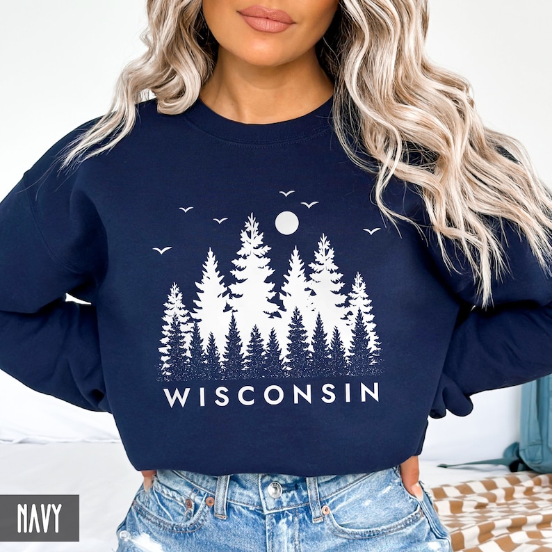 May include: A navy blue sweatshirt with a white graphic of a forest scene with trees, a moon, and birds. The text "WISCONSIN" is printed below the graphic.