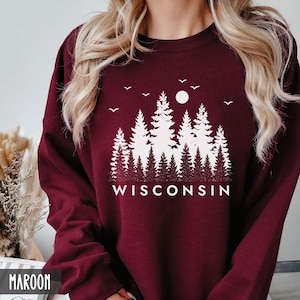 May include: Maroon sweatshirt with a white graphic of a forest silhouette and the word "WISCONSIN" printed below.