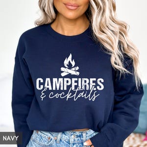 May include: Navy blue sweatshirt with a white graphic of a campfire and the words "Campfires & cocktails". The sweatshirt is a crew neck style and is made of a soft material. The word "NAVY" is in the bottom left corner.