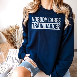 Pu&ograve; includere: Una felpa blu navy con la scritta "Nobody Cares Train Harder" stampata in bianco sul davanti.