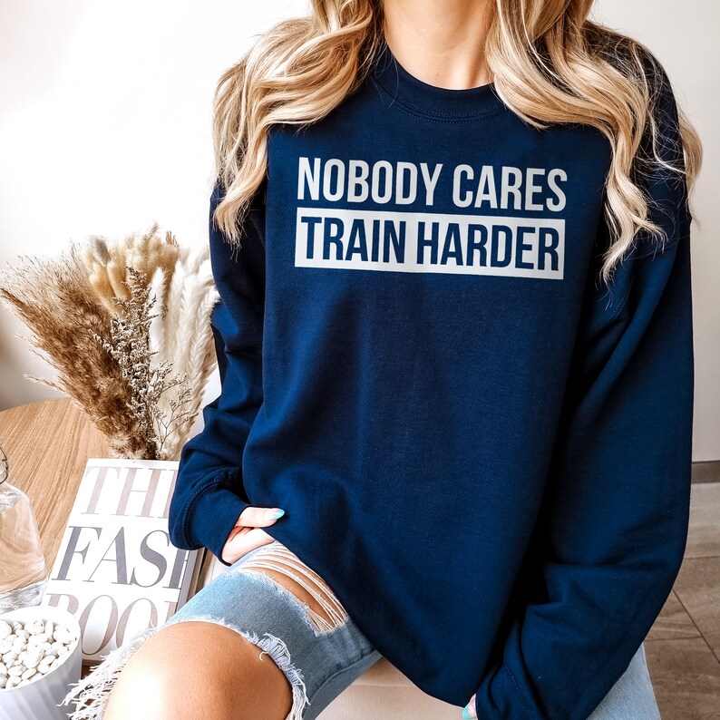 Pu&ograve; includere: Una felpa blu navy con la scritta "Nobody Cares Train Harder" stampata in bianco sul davanti.