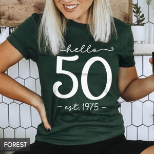 May include: A dark green t-shirt with white text that says "hello 50 - est. 1975 - "