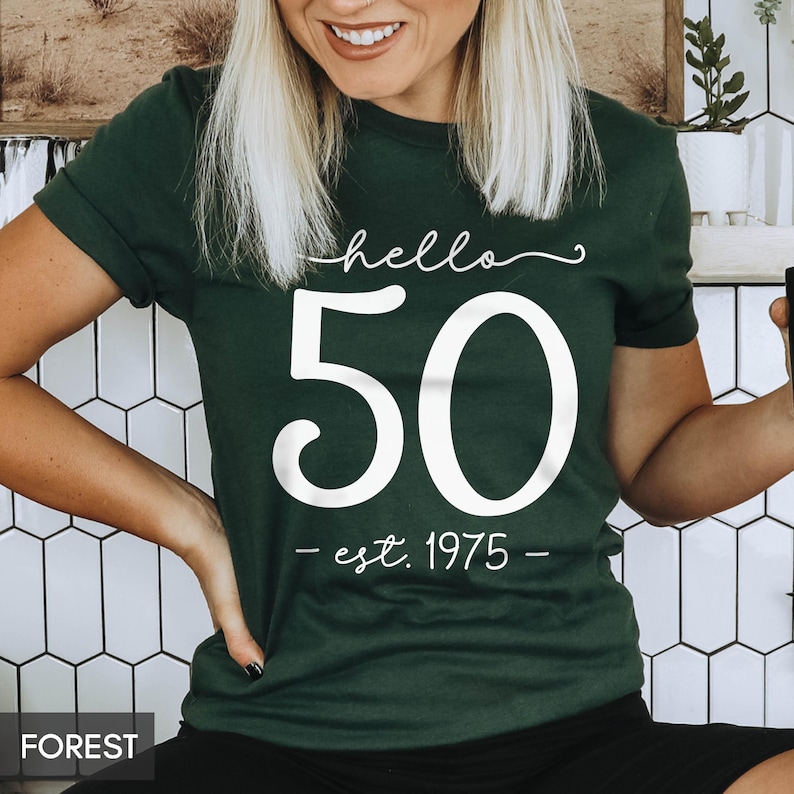 May include: A dark green t-shirt with white text that says "hello 50 - est. 1975 - "