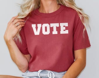 May include: A crimson red t-shirt with the word "VOTE" printed in white on the front.
