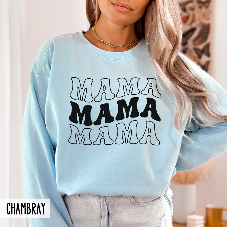 May include: A light blue sweatshirt with the text "MAMA" repeated three times in a retro font. The text is black and outlined in white.