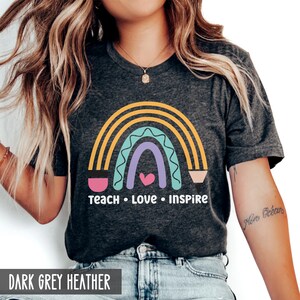 May include: A dark grey heather t-shirt with a rainbow design and the text "Teach Love Inspire".