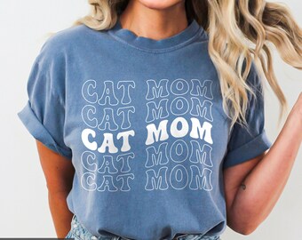 May include: A blue jean t-shirt with the text "CAT MOM" repeated five times in a stacked, retro-style font.