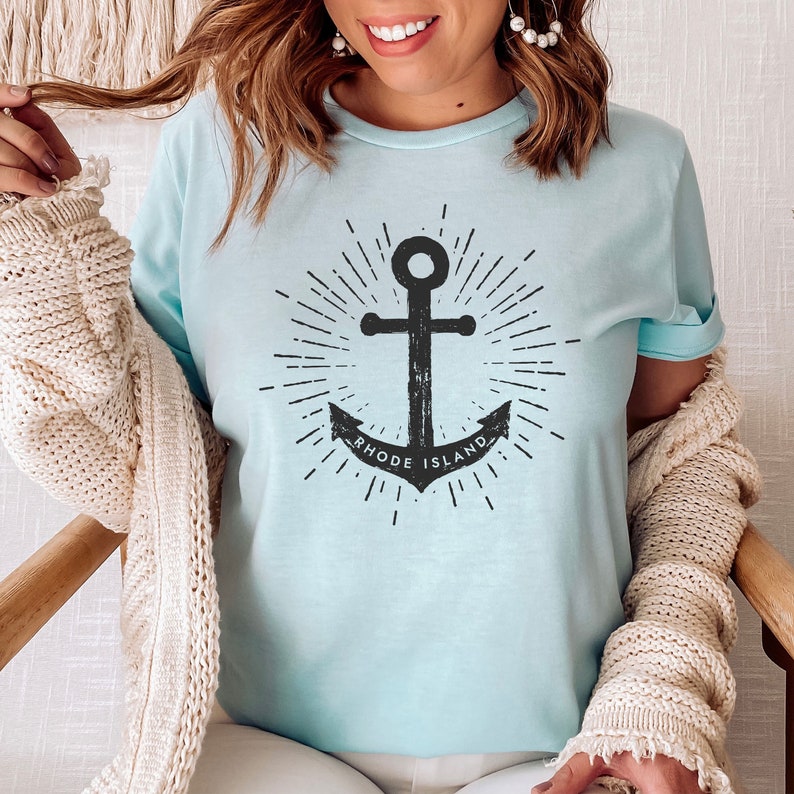 May include: A light blue t-shirt featuring a black anchor graphic and the text "Rhode Island".
