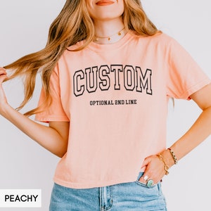 May include: Peachy colored cropped t-shirt with black text that reads "CUSTOM" and "OPTIONAL 2ND LINE".