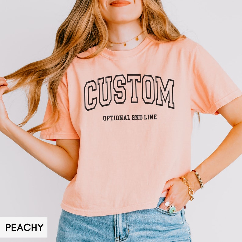 May include: Peachy colored cropped t-shirt with black text that reads "CUSTOM" and "OPTIONAL 2ND LINE".