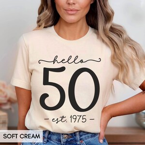 May include: A cream colored t-shirt with black text that reads "hello 50 - est. 1975 - "