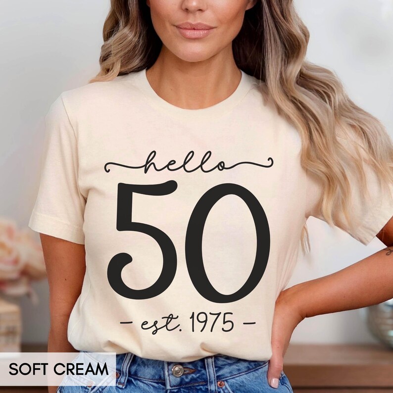 May include: A cream colored t-shirt with black text that reads "hello 50 - est. 1975 - "
