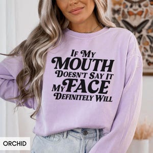 Puede incluir: Sudadera color orqu&iacute;dea con el texto negro "If My Mouth Doesn't Say It My Face Definitely Will". La sudadera es de cuello redondo.