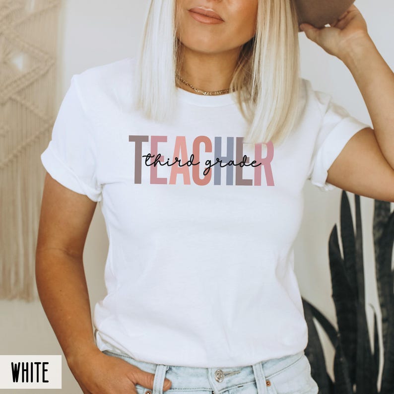 A woman modeling a white t-shirt with multicolored block letters spelling teacher overlaid with black cursive text reading third grade.
