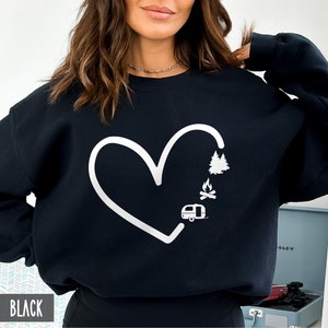 May include: Black sweatshirt with a white heart design. The heart is filled with a camper, a campfire, and a pine tree.