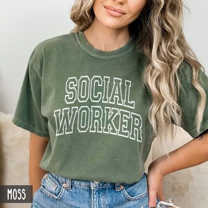Puede incluir: Una camiseta verde musgo con el texto "SOCIAL WORKER" en letras blancas con contorno.
