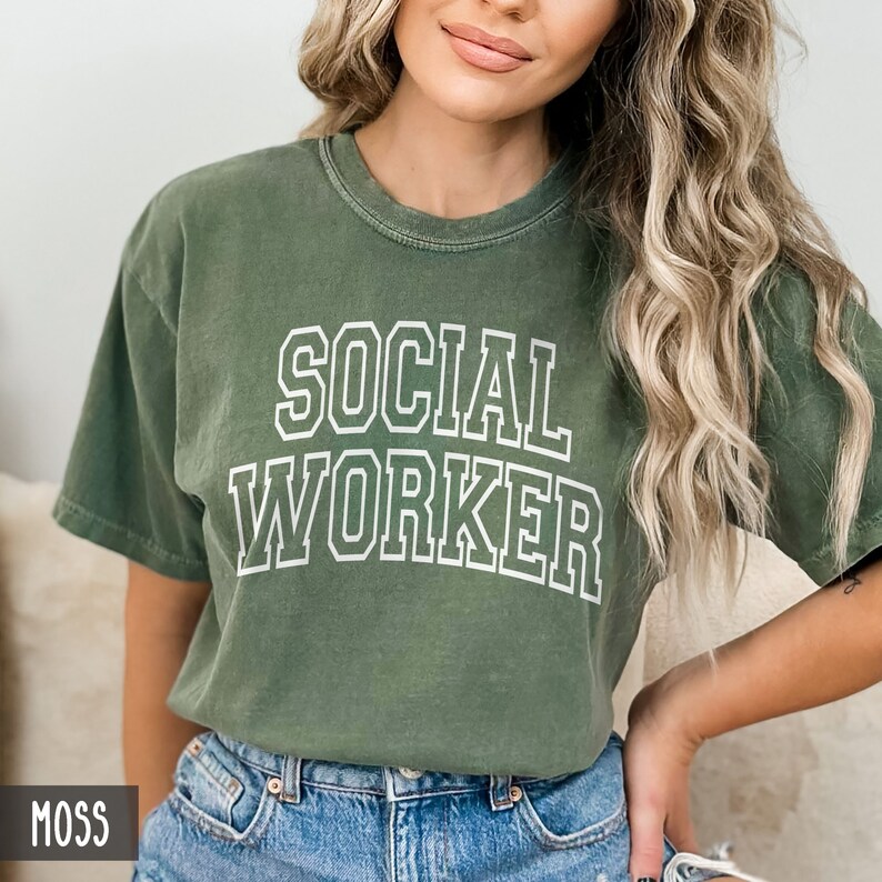 Puede incluir: Una camiseta verde musgo con el texto "SOCIAL WORKER" en letras blancas con contorno.