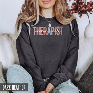 May include: A dark heather grey sweatshirt with the text "THERAPIST mental health" in colorful lettering.