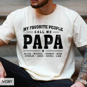A man wearing a white t-shirt with the text "MY FAVORITE PEOPLE CALL ME PAPA" printed on it.