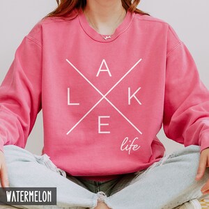 May include: A pink sweatshirt with a white graphic design that says "LAKE life" with the letters "LAKE" in a criss-cross pattern.