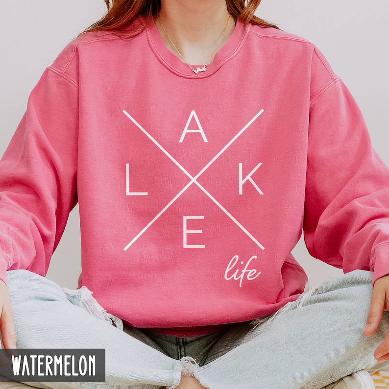 May include: A pink sweatshirt with a white graphic design that says "LAKE life" with the letters "LAKE" in a criss-cross pattern.