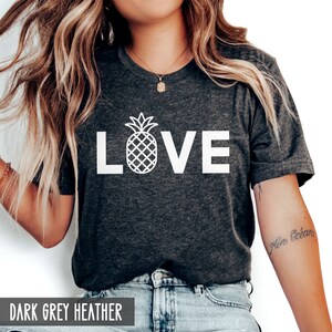 May include: A dark grey heather t-shirt with the word "LOVE" in white text. A white pineapple graphic is in the center of the word "LOVE".