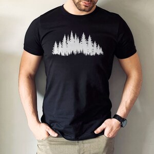 May include: A black t-shirt with a white silhouette of a forest on the front.
