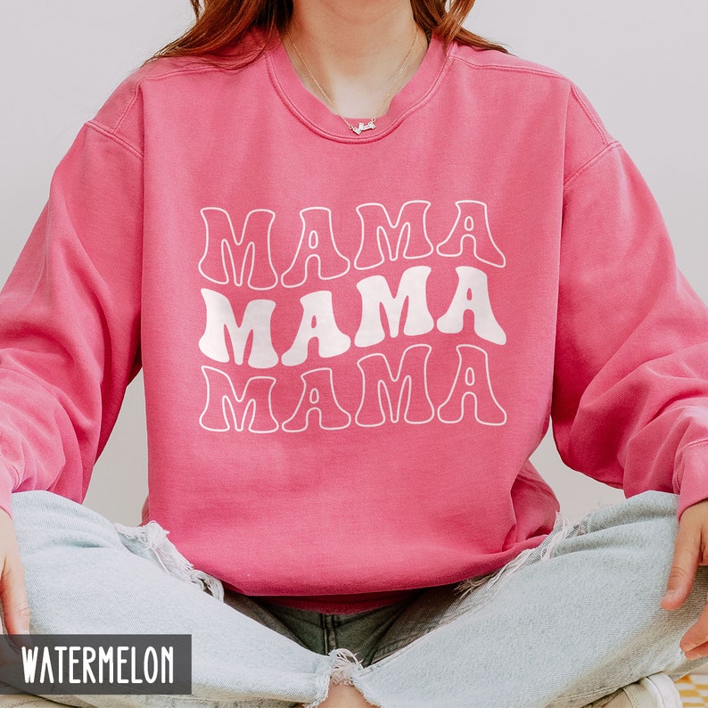 May include: A pink sweatshirt with the words "Mama Mama Mama" in white, retro-style lettering. The sweatshirt is made of a soft, comfortable material and has a relaxed fit.