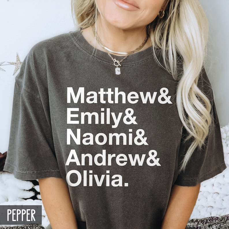 K&ouml;nnte beinhalten: Ein dunkelgraues T-Shirt mit wei&szlig;em Text, der "Matthew & Emily & Naomi & Andrew & Olivia." lautet.