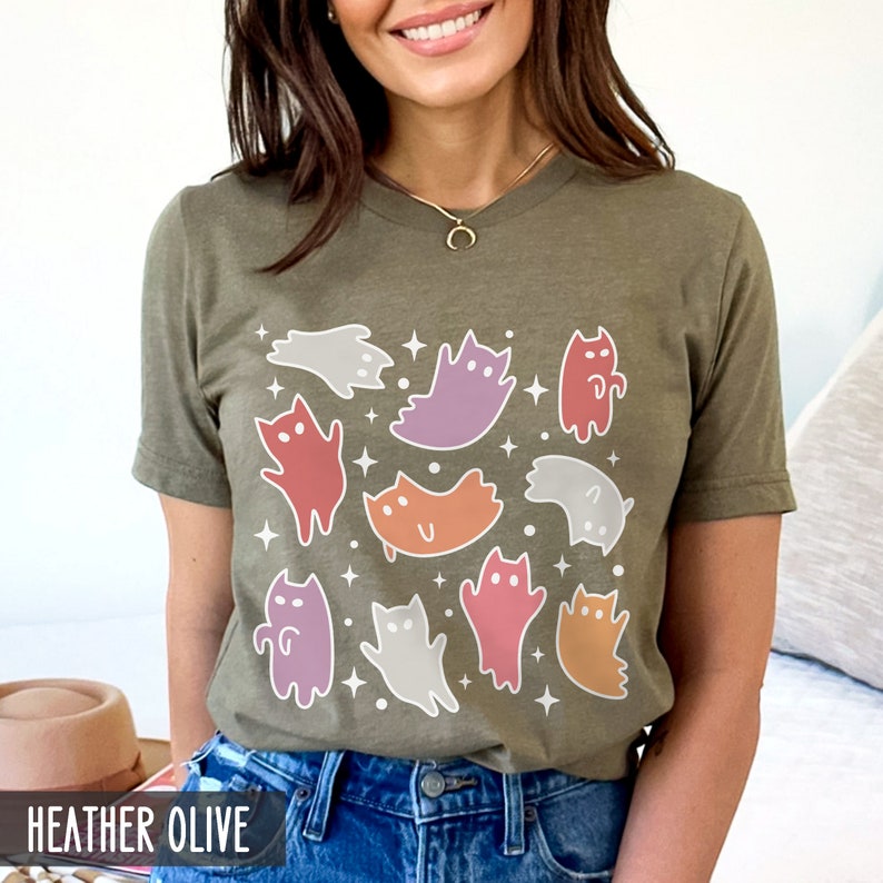 Op de afbeelding: Een heide olijfkleurig t-shirt met een grafische print van kleurrijke spookkatten. De grafiek bevat een verscheidenheid aan pastelkleuren, waaronder paars, oranje, roze en rood.