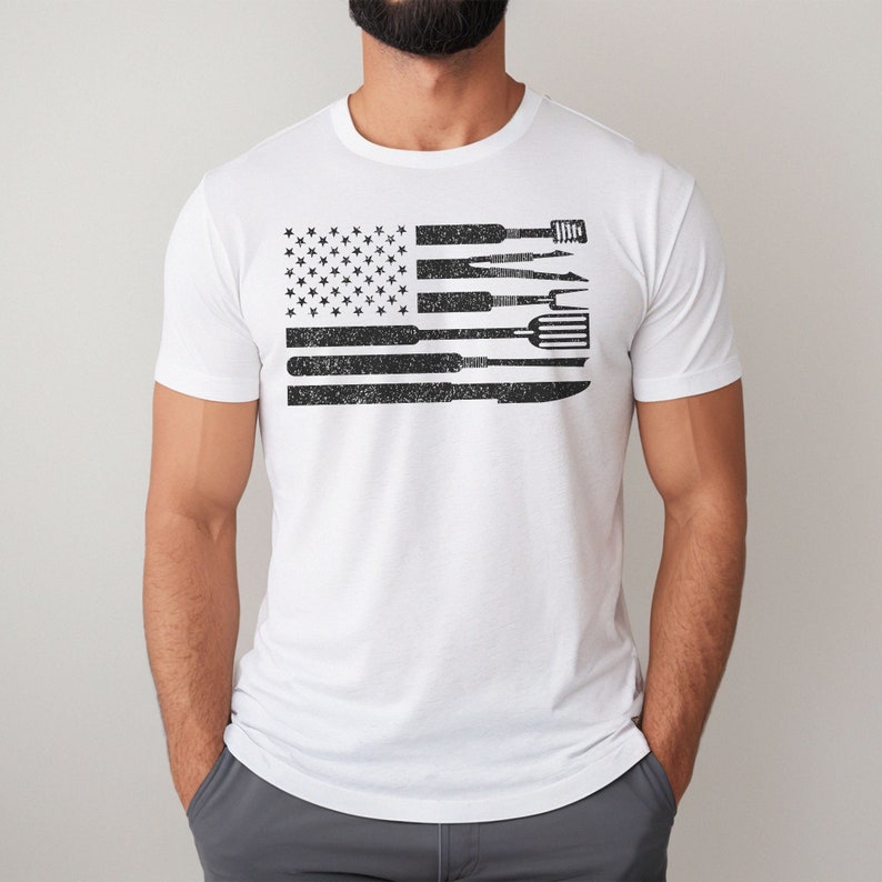 Puede incluir: Camiseta blanca con un dise&ntilde;o de bandera americana en blanco y negro. La bandera est&aacute; compuesta por herramientas, como una esp&aacute;tula, un cuchillo y un tenedor.