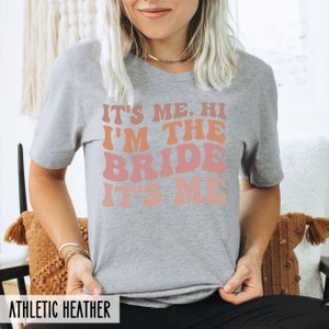 May include: A gray t-shirt with the text "It's Me. Hi I'm The Bride It's Me" in a rainbow gradient font.