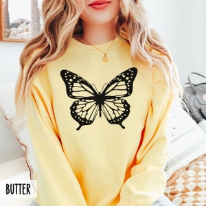 Peut inclure: Un sweat-shirt jaune avec un motif de papillon noir sur le devant. Le papillon a des ailes noires et blanches.