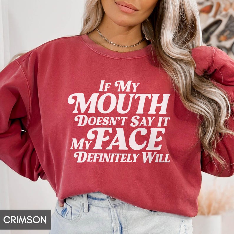 Puede incluir: Sudadera de color carmes&iacute; con el texto "IF MY MOUTH DOESN'T SAY IT MY FACE DEFINITELY WILL" en blanco, en negrita, con fuente serif. La sudadera es de cuello redondo y tiene mangas largas. La palabra "CRIMSON" est&aacute; en un cuadro blanco en la parte inferior izquierda.
