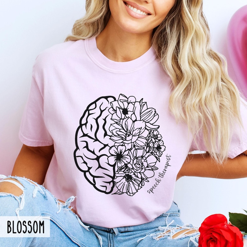 May include: A pink t-shirt with a black and white design of a brain and flowers. The text "Speech Therapist" is written on the shirt.