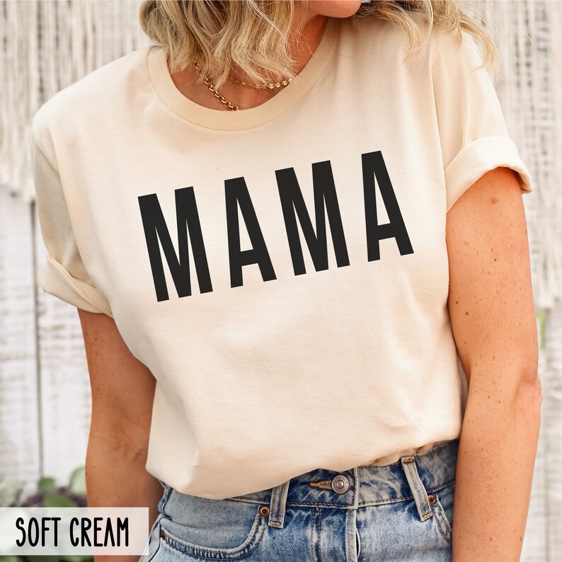 May include: A soft cream colored t-shirt with the word "MAMA" printed in black on the front.