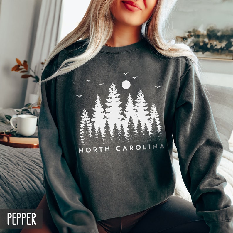 May include: A dark gray sweatshirt with a white graphic design of a forest silhouette with a full moon and the text "NORTH CAROLINA".