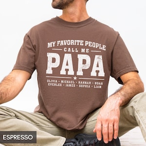 A man wearing a brown t-shirt with the text "MY FAVORITE PEOPLE CALL ME PAPA" printed on it.