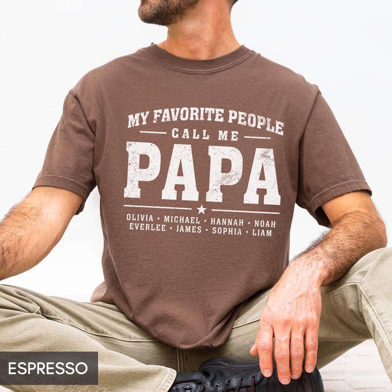A man wearing a brown t-shirt with the text "MY FAVORITE PEOPLE CALL ME PAPA" printed on it.
