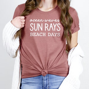 May include: A mauve t-shirt with the text "ocean waves SUN RAYS BEACH DAYS" in white.