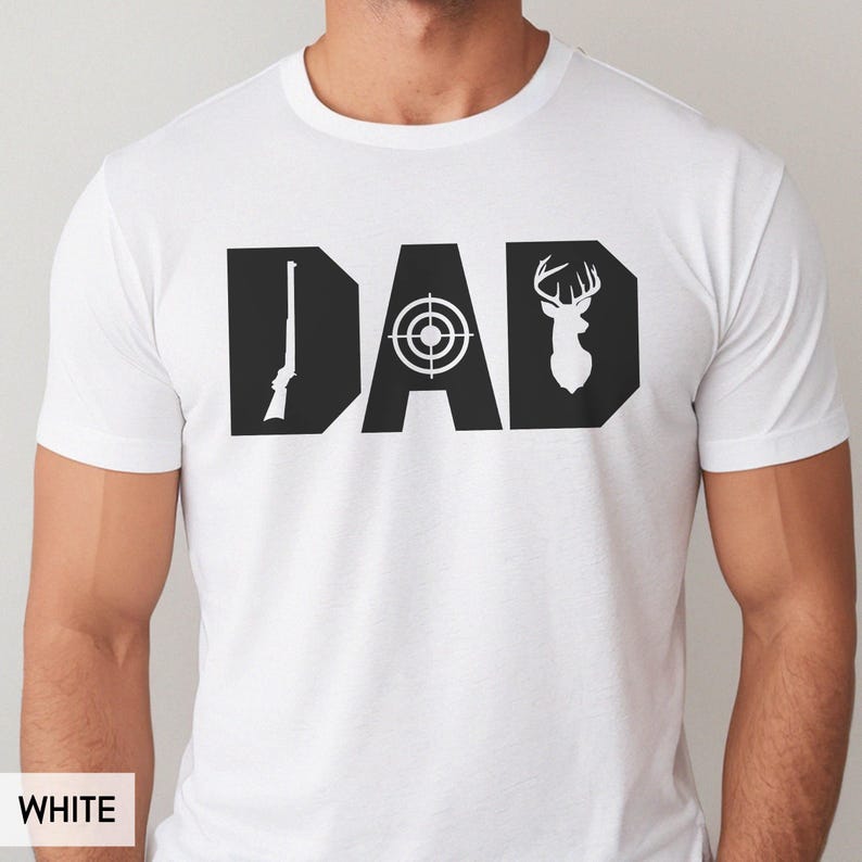 May include: White t-shirt with a black graphic design that spells out "DAD". The letter "D" features a rifle, the "A" has a target, and the final "D" has a deer silhouette. The shirt is made of a soft material.