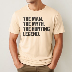 May include: A beige t-shirt with the text "THE MAN. THE MYTH. THE HUNTING LEGEND." printed in black.