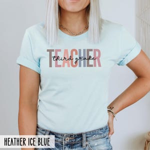 A woman in a heather ice blue t-shirt displaying multicolored block letters spelling teacher and black cursive text reading third grade.