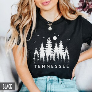 May include: Black t-shirt with a white graphic of a forest silhouette and the word "TENNESSEE" printed below.