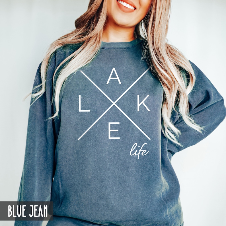 May include: A blue jean sweatshirt with white text that reads "LAKE life" with the letters "LAKE" forming a cross.