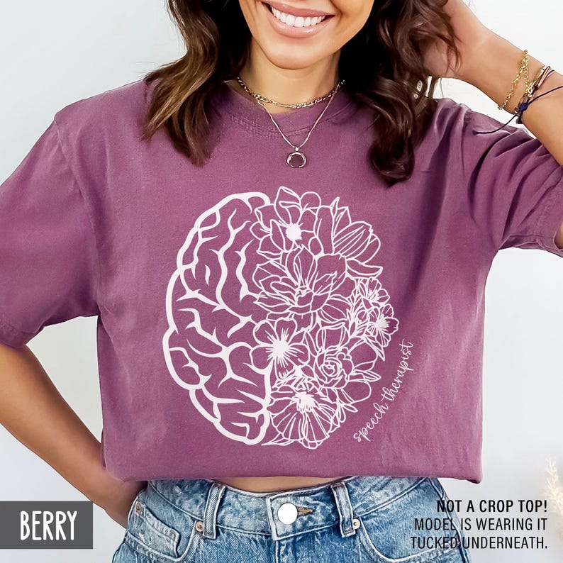 May include: A purple t-shirt with a white outline of a brain and flowers. The text "Speech therapist" is written on the shirt.