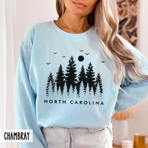 May include: Light blue sweatshirt with a black silhouette of a forest and the text "NORTH CAROLINA".