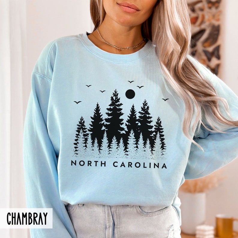May include: Light blue sweatshirt with a black silhouette of a forest and the text "NORTH CAROLINA".