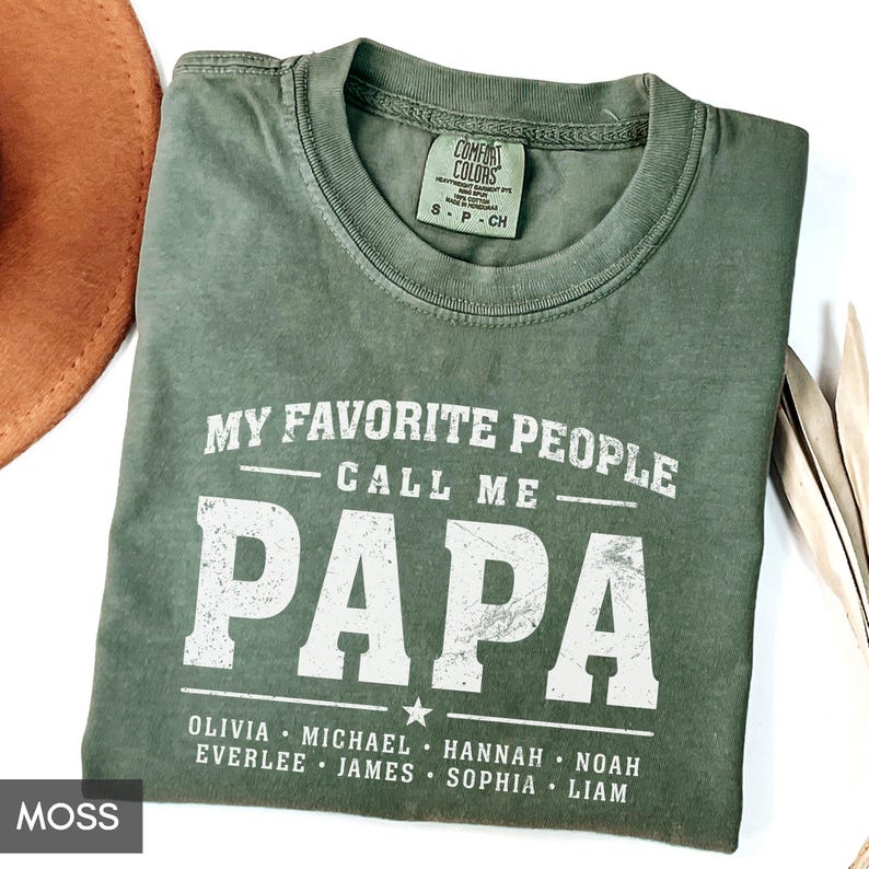 A green t-shirt with the text "MY FAVORITE PEOPLE CALL ME PAPA" printed on it, along with the names "Olivia, Michael, Hannah, Noah, Everlee, James, Sophia, Liam" below it.