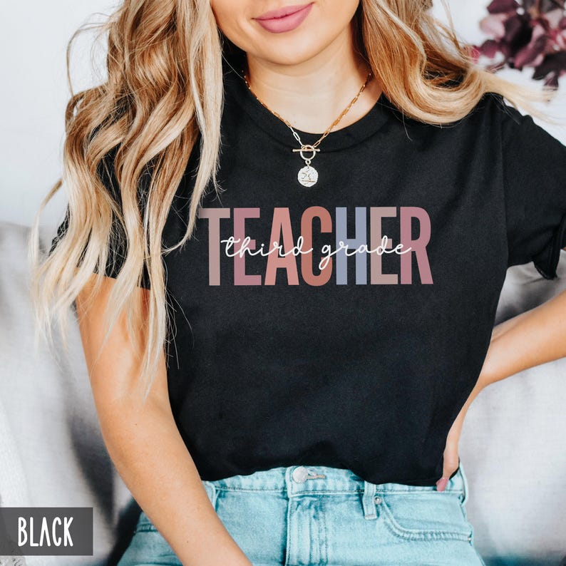 A woman wearing a black t-shirt featuring pastel block letters spelling teacher and white cursive text that reads third grade.